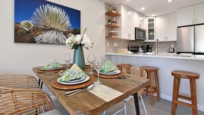 Un comedor con una mesa de madera dispuesta para cuatro personas, rodeada de sillas de mimbre. Un cuadro grande de una planta del desierto cuelga en la pared.