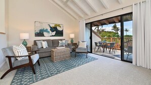 Un salón con un sofá gris, dos sillones, una mesa de centro y un cuadro grande en la pared. Hay una puerta corredera de vidrio que da a un patio exterior con una mesa y sillas.
