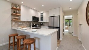 Una cocina moderna con armarios blancos, una isla central con taburetes, un microondas y un refrigerador de acero inoxidable.