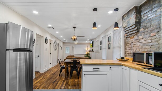 Una cocina moderna con armarios blancos, encimera de madera, electrodomésticos de acero inoxidable y una pared decorativa de piedra.