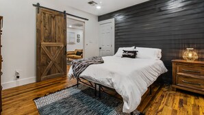 Un dormitorio con cama, mesita de noche, piso de madera, ventilador de techo y puerta corrediza de estilo rústico.