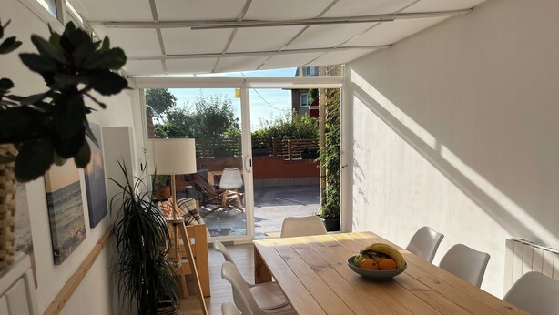 A dining area with a wooden table, white chairs, and a bowl of fruit. There are potted plants and a view of the outside. - "Amaluz Ocean Villa Bilbao Beach for families and groups of friends". (Getxo)
