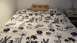 Un dormitorio con una cama que tiene un edredón con motivos marinos, un mural de un pulpo en la pared y una mesita de noche con una lámpara.