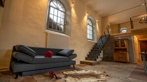 A spacious living room with a grey sofa, a fur rug, and a staircase leading to an upper level.