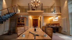 A dining area with a wooden table, chairs, a chandelier, and a staircase leading to an upper level.