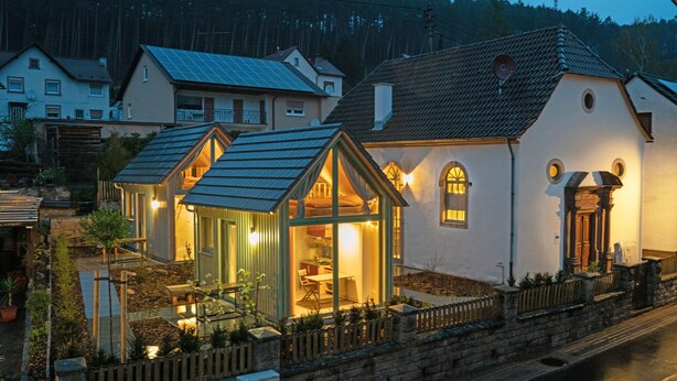 A house with a glass conservatory, a dining area, and a kitchen visible through the conservatory.