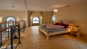 A spacious room with a large bed, wooden flooring, and a balcony with a railing.