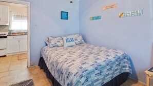 Una camera da letto con un letto con copriletto a tema spiaggia, un angolo cottura con mobili bianchi e un cartello che indica una casa sulla spiaggia.