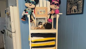 Una cucina con un frigorifero bianco, un muro blu e uno scaffale con asciugamani piegati e peluche di Topolino.