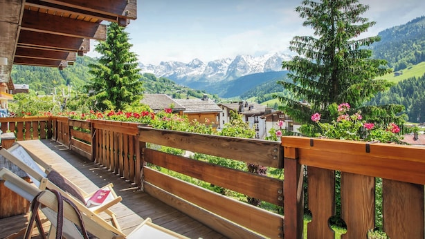 A wooden deck with a view of a mountain range, wooden benches, and potted plants.