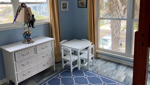 A room with a white dresser, a small table, and two chairs. There are two windows with curtains, and a view of the outside. - 3 bed/2 bath private oceanfront home with direct beach access on Amelia Island! (fernandina beach)