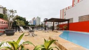 En tagterrasse med swimmingpool, et overdækket opholdsområde, plantekasser og udsigt til byens skyline.