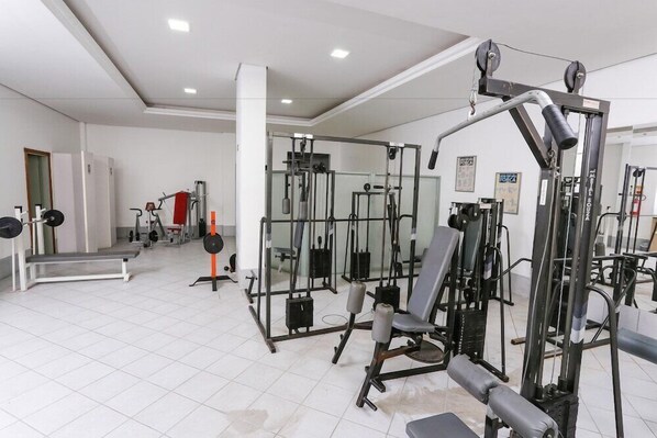 A gym with various exercise machines, a weight bench, and a mirrored wall. - Hotel Suarez Executive (Novo Hamburgo)