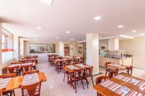 Un comedor de hotel con varias mesas y sillas, una zona de cocina y un mostrador de recepción.