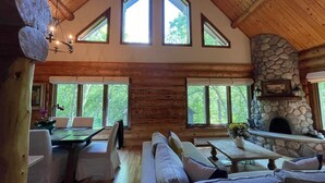 A spacious living room with a high wooden ceiling, large windows, a stone fireplace, and a cozy seating area.