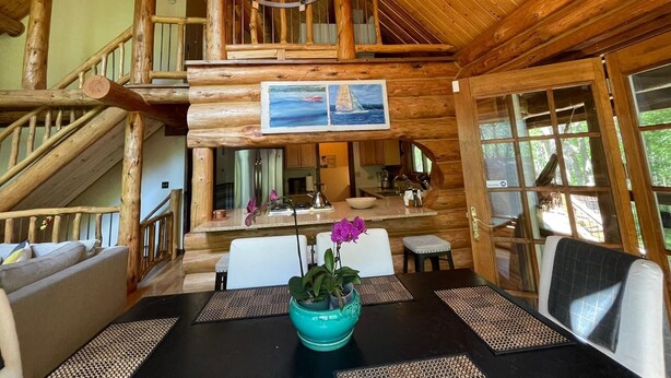 A wooden cabin interior with a dining area, a staircase, and a painting on the wall.