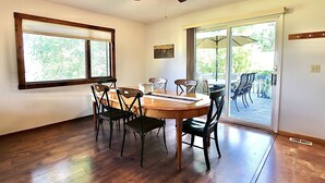 Ein Essbereich mit Holztisch und -stühlen, einem Deckenventilator und einer Glastür, die auf eine Außenpatio führt.