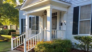 A two-story house with a front porch, a small garden, and a flag on the left.