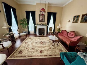 En traditionel stue med pejs, en rød sofa, et mønstret tæppe og klassiske møbler.