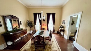 A dining room with a large table, chairs, a chandelier, and a mirror on the wall.