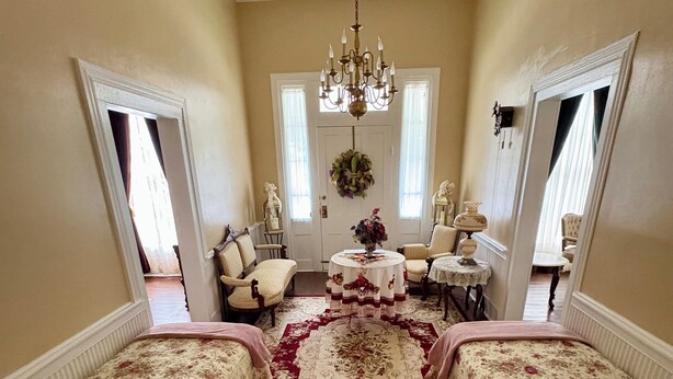 A room with a chandelier, floral-patterned bedding, a central rug, and a mirror on the wall.