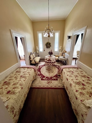A room with a chandelier, floral-patterned bedding, a central rug, and a mirror on the wall.