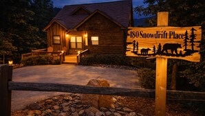Una cabaña de madera con un letrero que dice '180 Snowdrift Place' y siluetas de árboles y animales.
