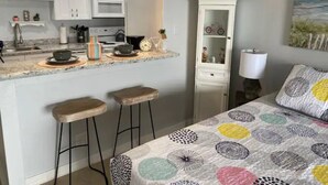 A modern kitchen with white cabinets, a microwave, and a countertop with stools. There is a cabinet with decorative items and a painting on the wall. - Great studio, wonderful amenities, OCEAN views! (Galveston)