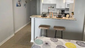 A modern kitchen with white cabinets, a granite countertop, and two bar stools. - Great studio, wonderful amenities, OCEAN views! (Galveston)
