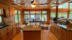Una cocina amplia con armarios de madera, una isla central y ventanas grandes que ofrecen vistas al exterior.
