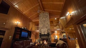Un salón amplio con chimenea de piedra, techo de madera y un televisor sobre un mueble.