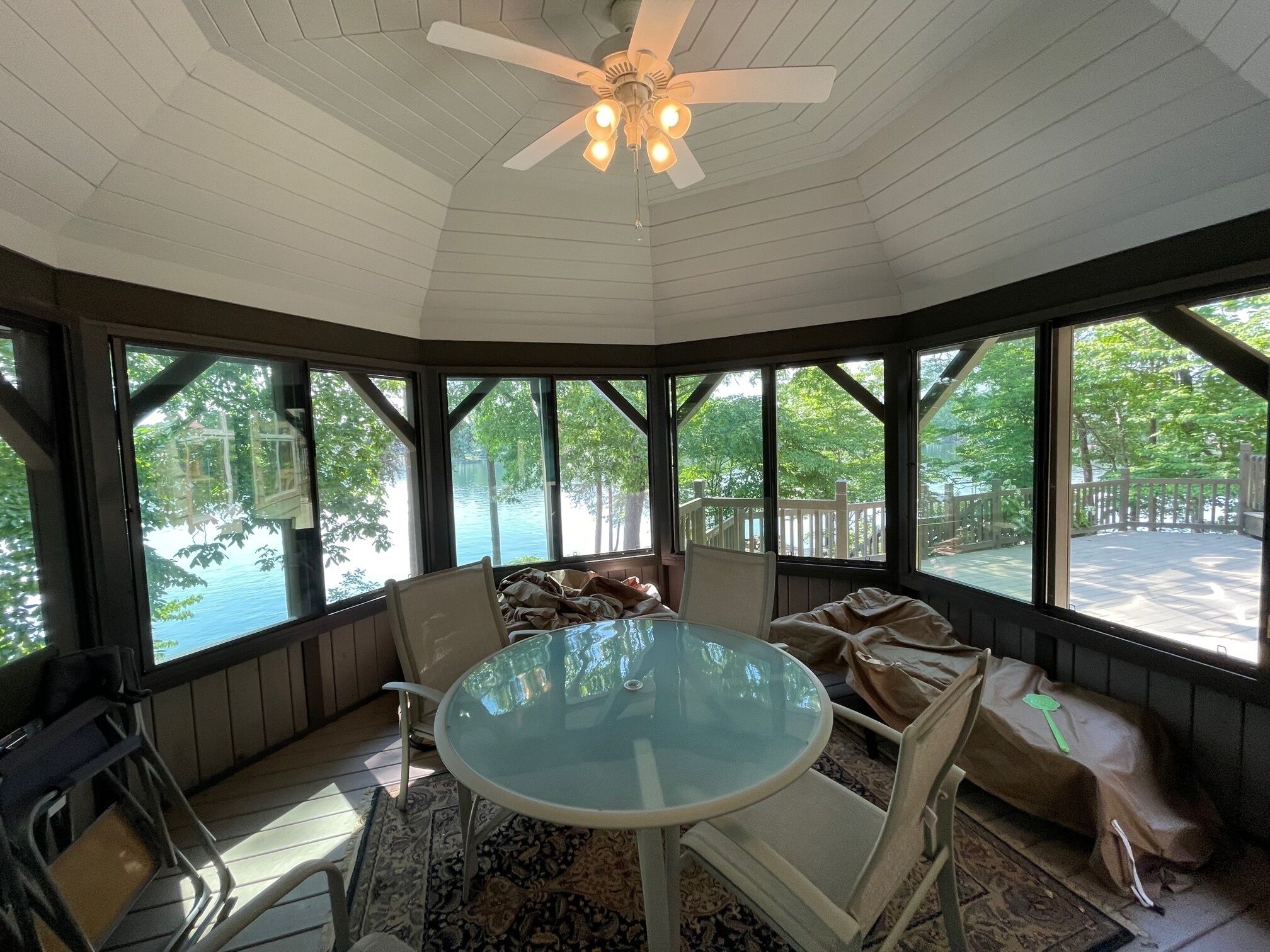 A sunroom with a glass table, chairs, and a ceiling fan.