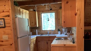 A wooden cabin kitchen with a refrigerator, sink, and wooden cabinets.