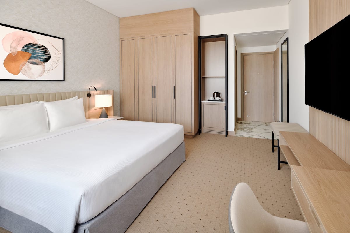 A hotel room with a large bed, a desk, a chair, a TV, and a wardrobe.