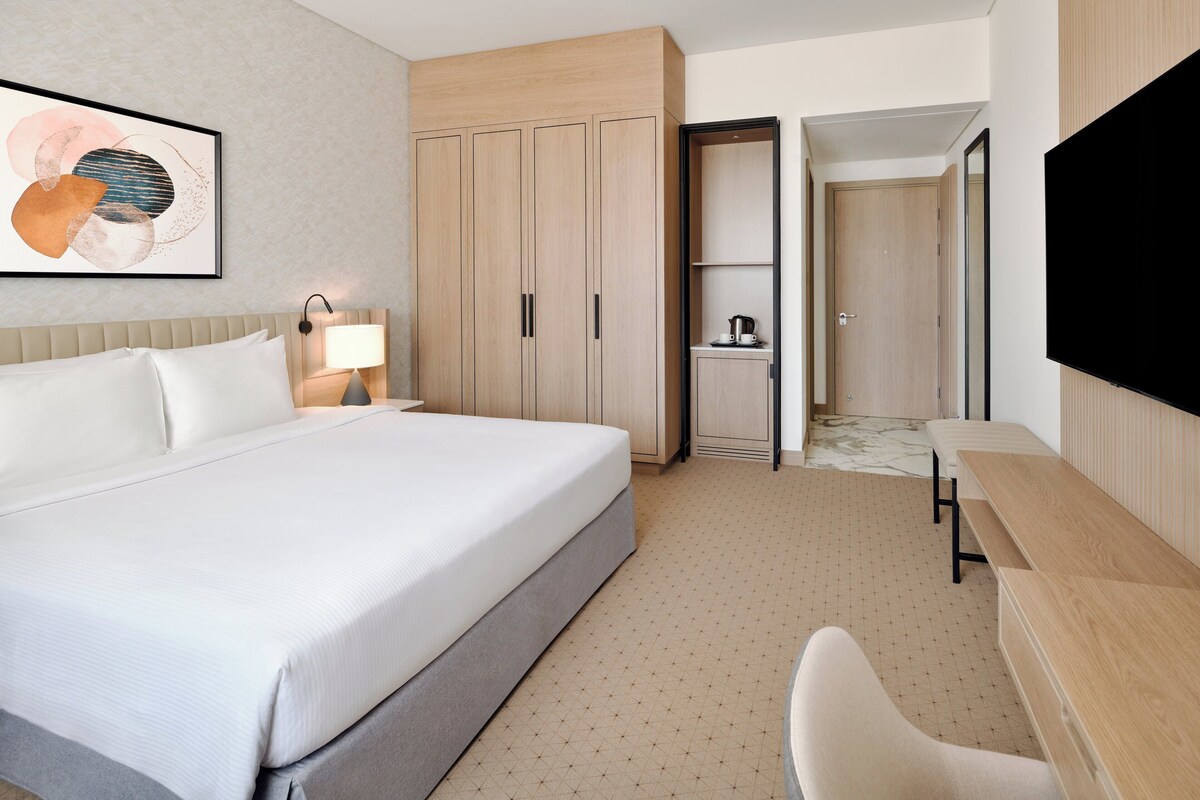 Una habitación de hotel con una cama grande, un escritorio, una silla, un televisor y un armario.