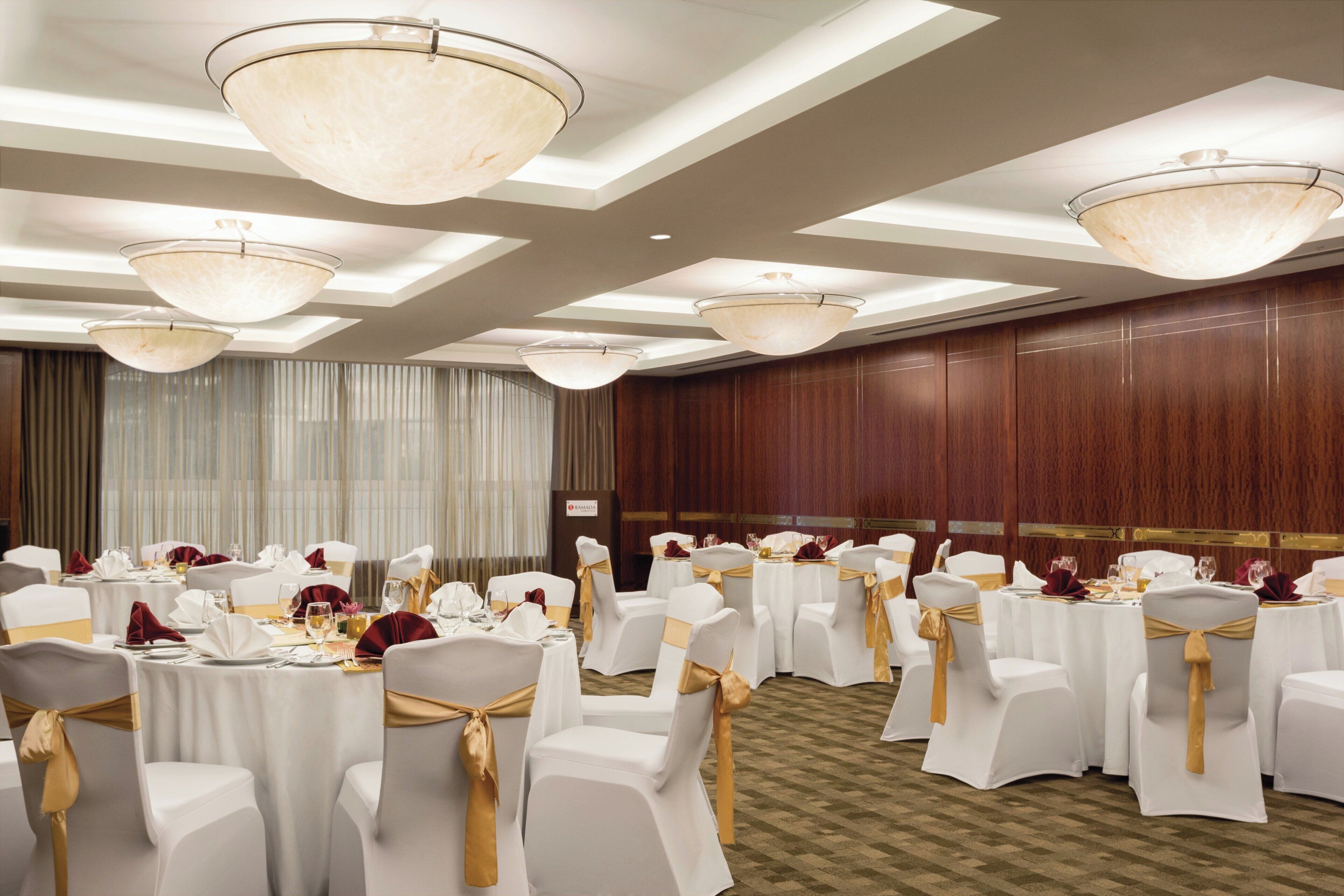 Un salón de banquetes con mesas redondas, sillas blancas con cintas doradas y grandes candelabros.