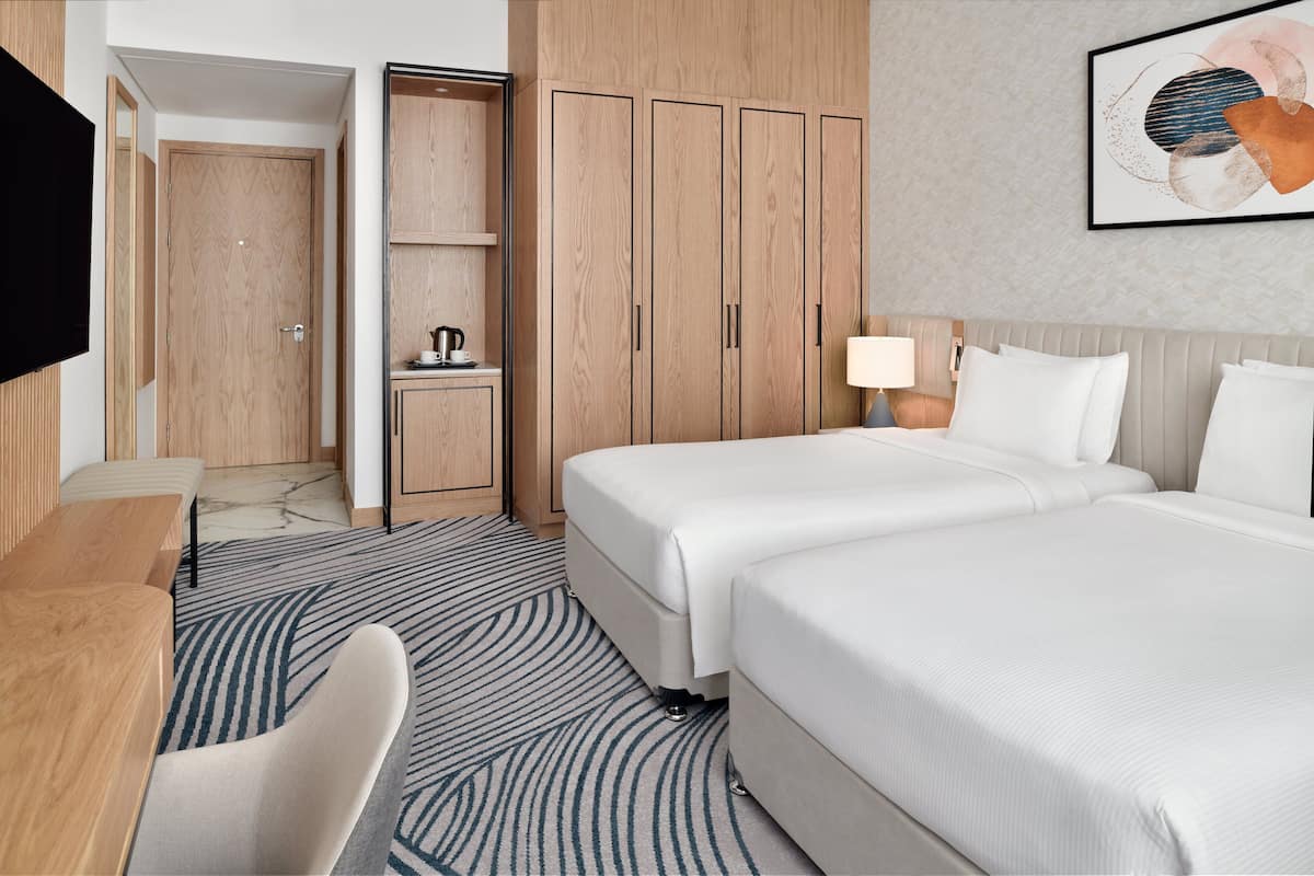 A hotel room with two beds, a desk, a chair, a wardrobe, and a television.