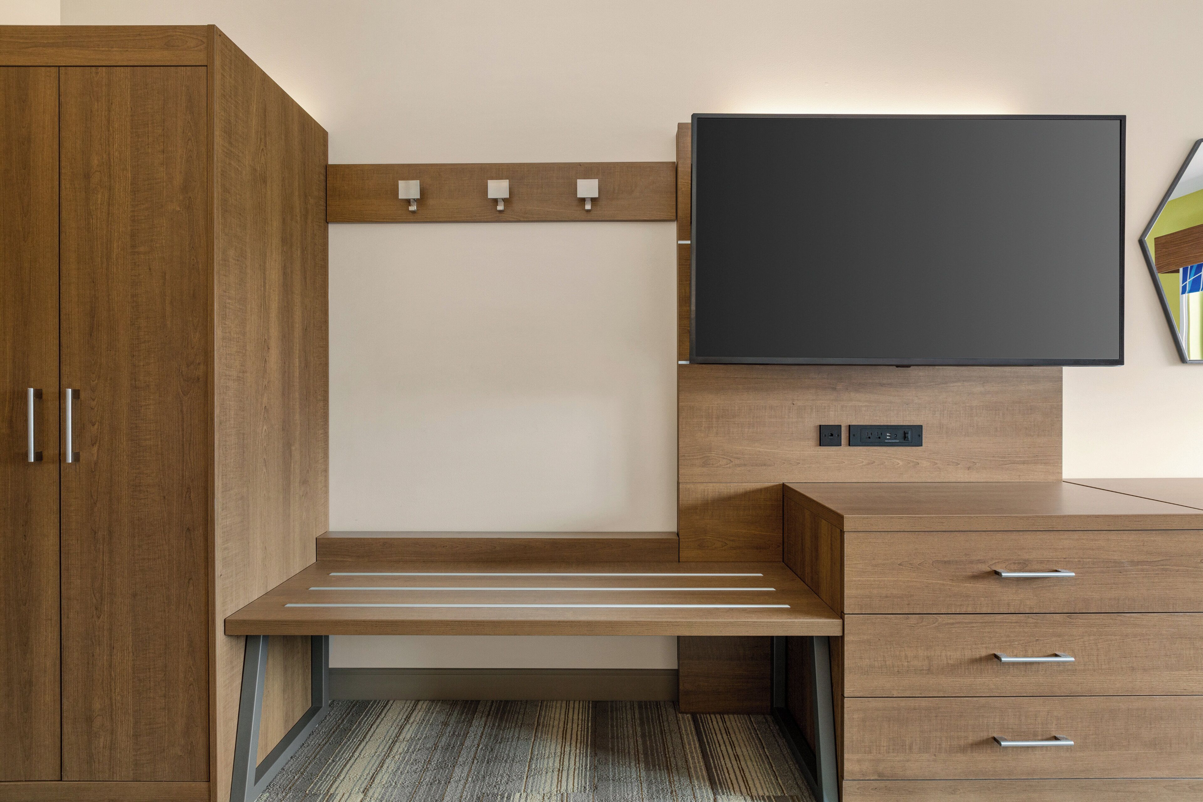 Een moderne slaapkamer met een houten garderobe, een bed met hoofdeinde, een nachtkastje en een flatscreen televisie aan de muur.