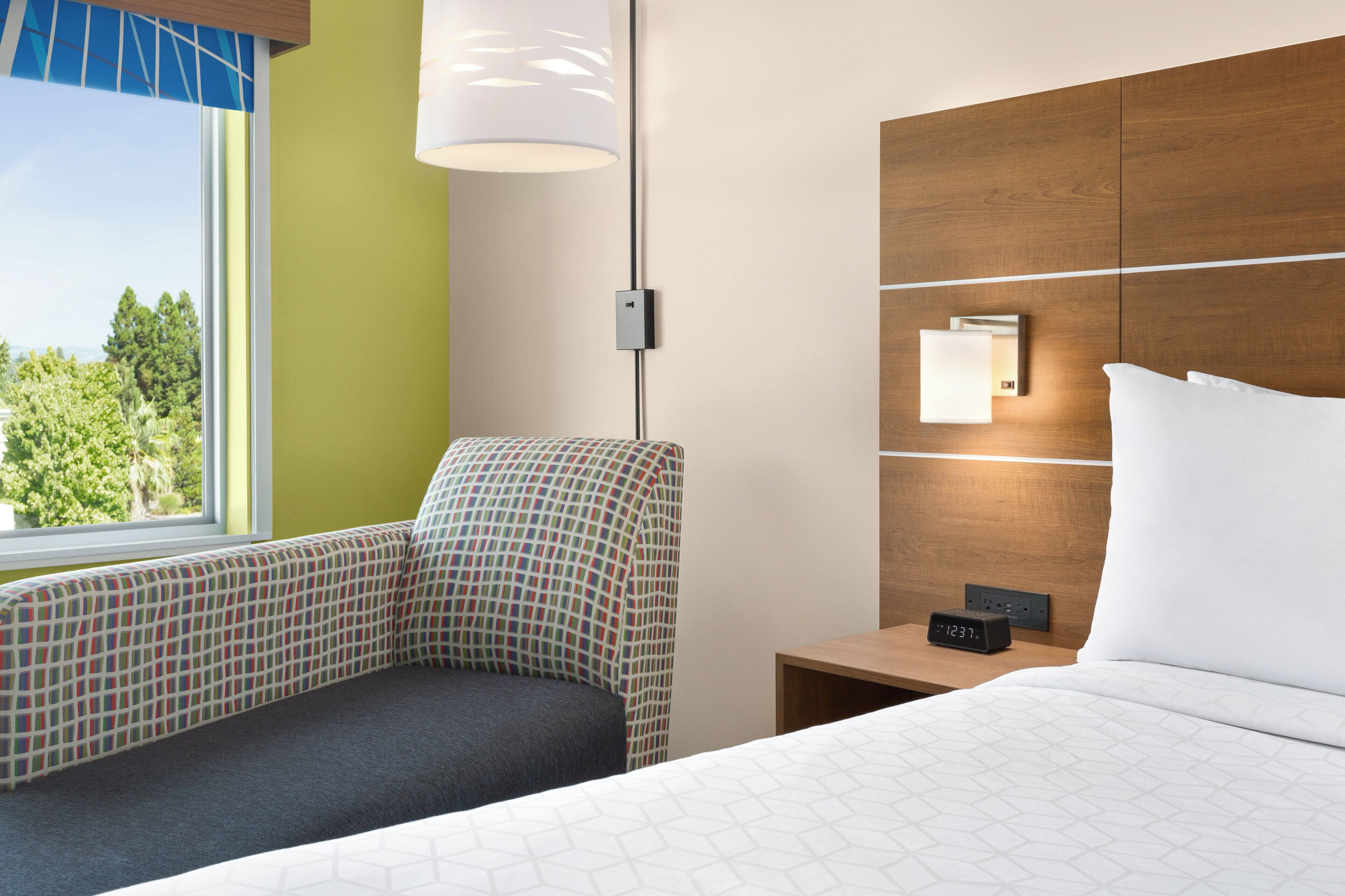 A hotel room with a bed, a nightstand, a lamp, and a chair.