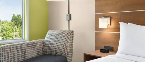 Una habitación de hotel con una cama, una mesita de noche, una lámpara y una silla.