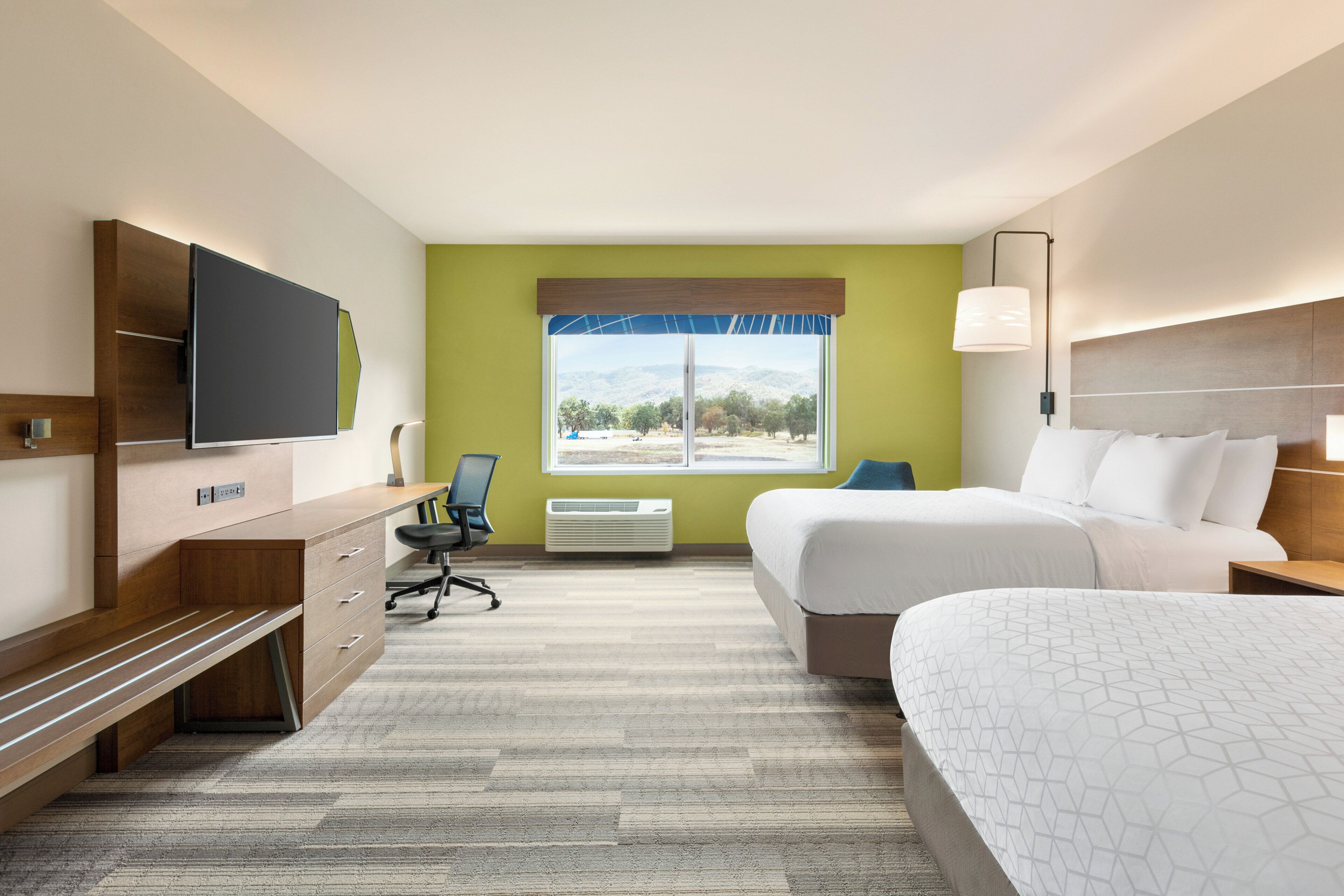 Une chambre d’hôtel équipée d’un lit, d’un bureau, d’une chaise, d’une télévision et d’une fenêtre donnant sur l’extérieur.