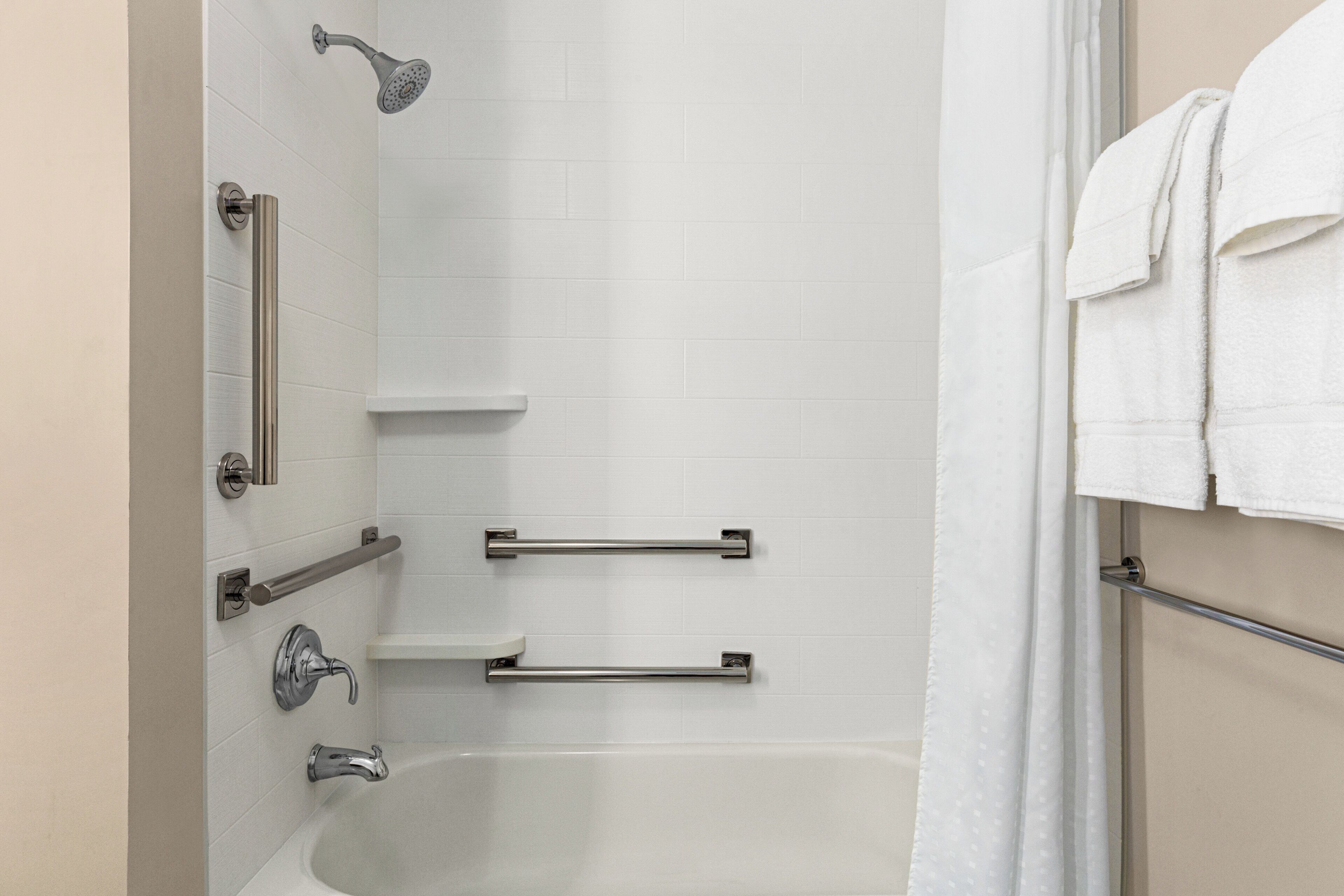 A bathroom with a bathtub, a shower, grab bars, and a towel rack.