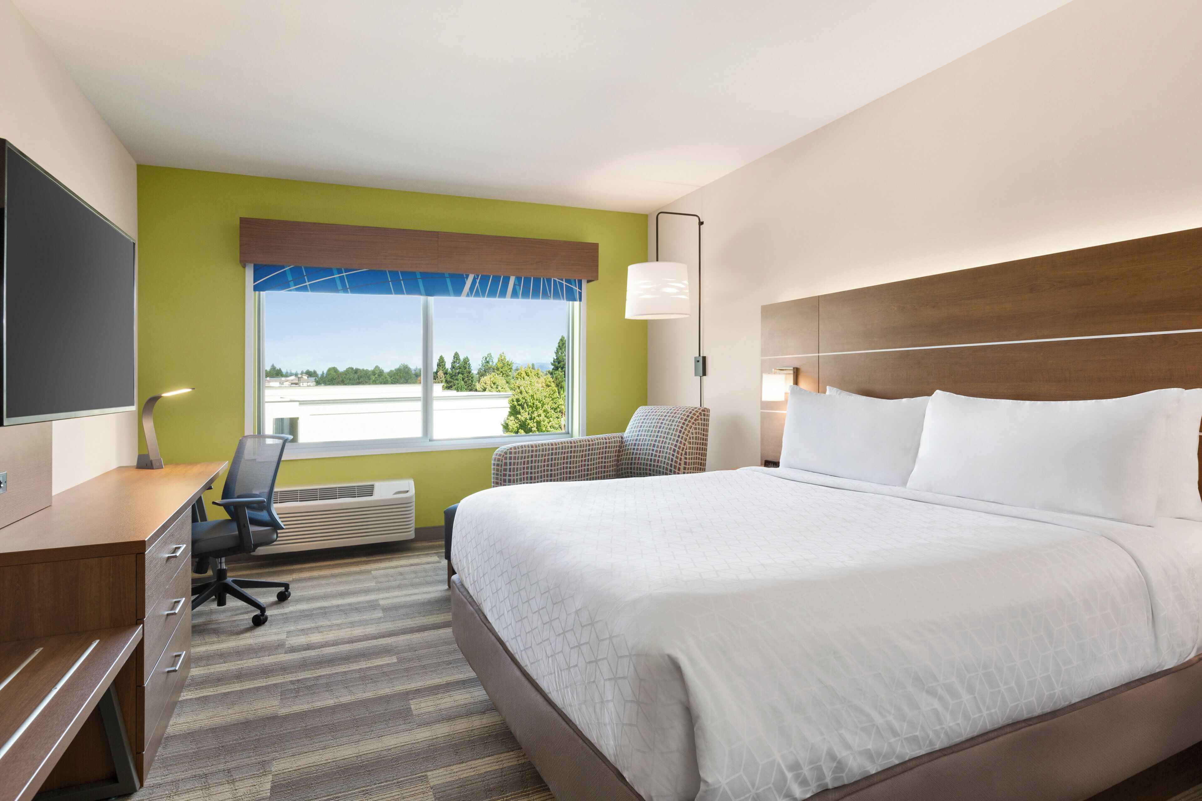 Une chambre d’hôtel avec un lit, un bureau, une chaise et une grande fenêtre.