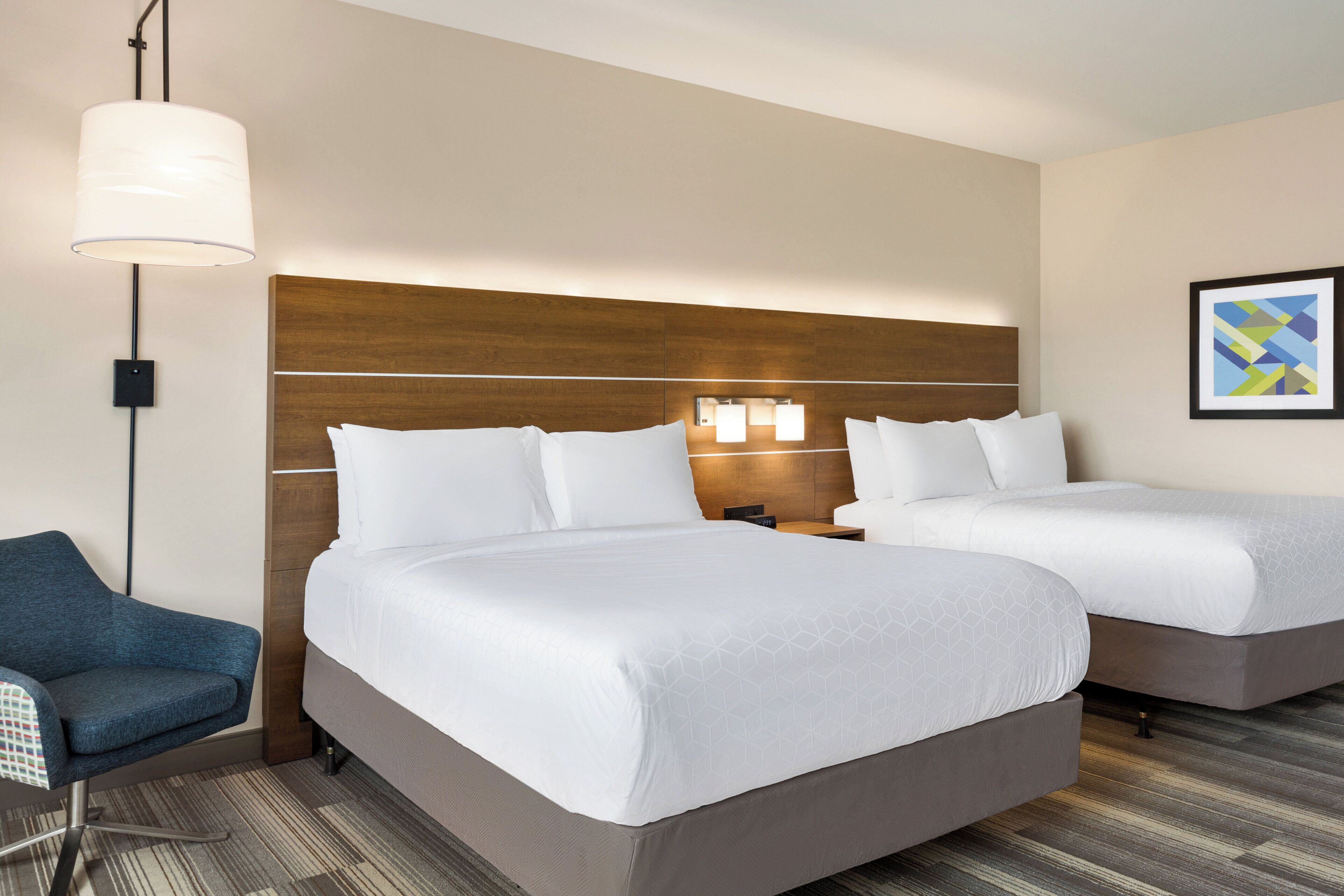 A hotel room with two beds, a desk, a chair, and a lamp.