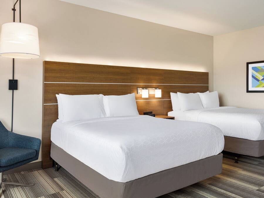 A hotel room with two beds, a desk, a chair, and a lamp.