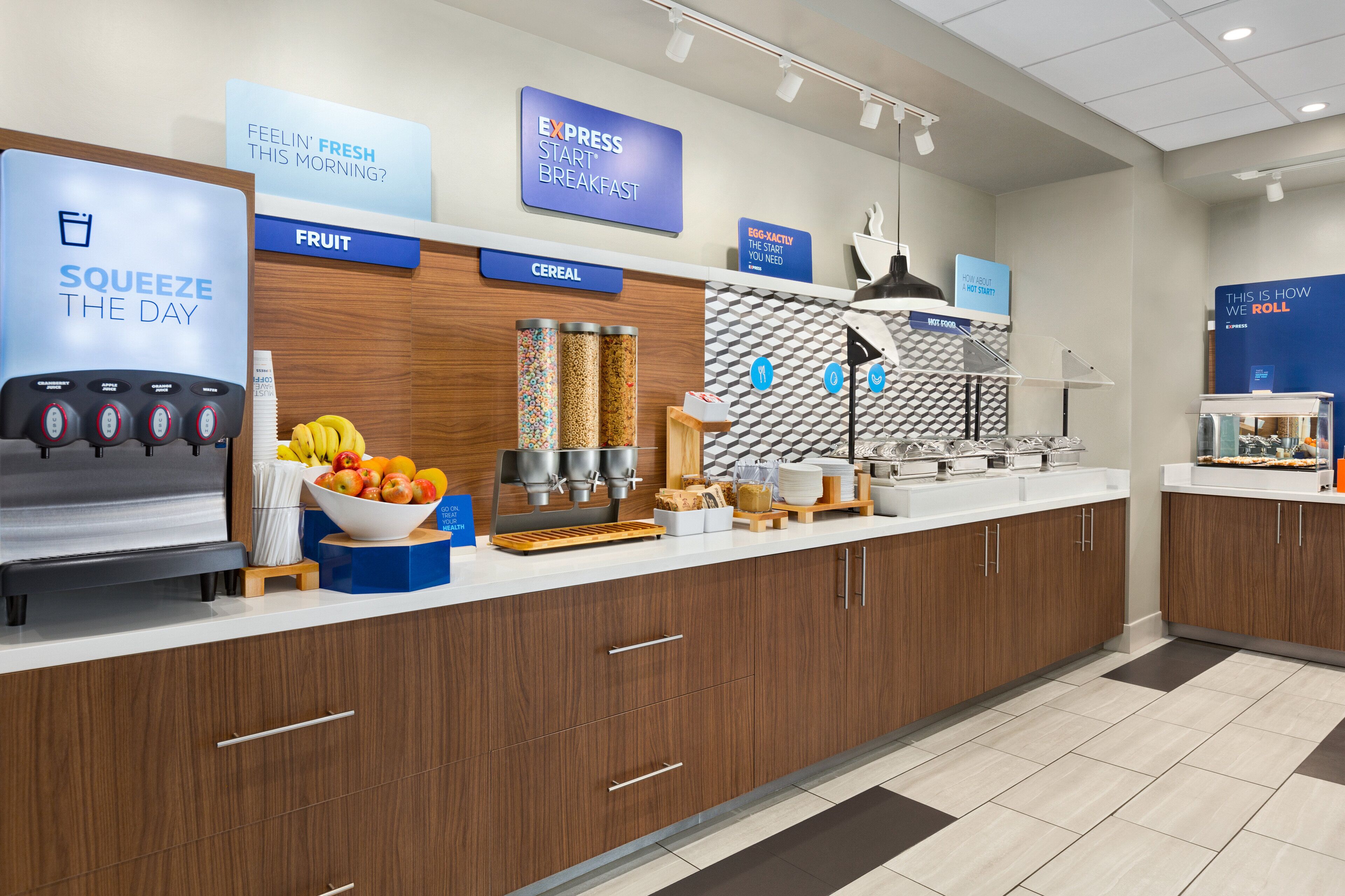 A modern breakfast area with a coffee machine, fruit bowl, cereal, and a sign for express breakfast.