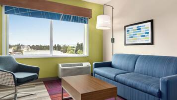 Ein modernes Hotelzimmer mit einem großen Fenster, einem blauen Sofa, einem Holztisch und einem gemusterten Teppich.