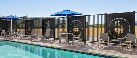 A poolside area with lounge chairs and umbrellas, surrounded by a fence with decorative panels.