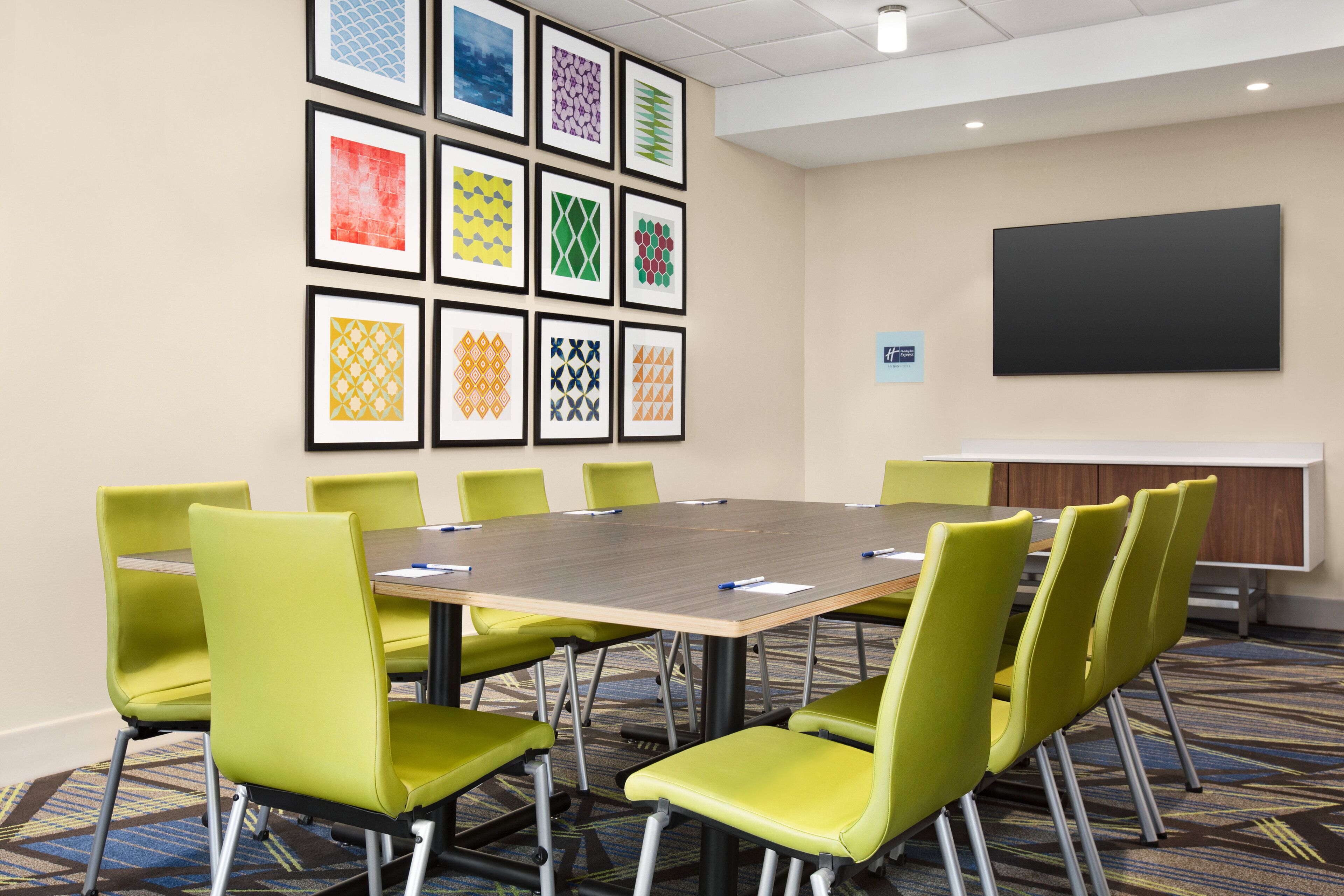 A conference room with a large table, green chairs, and framed artwork on the wall.