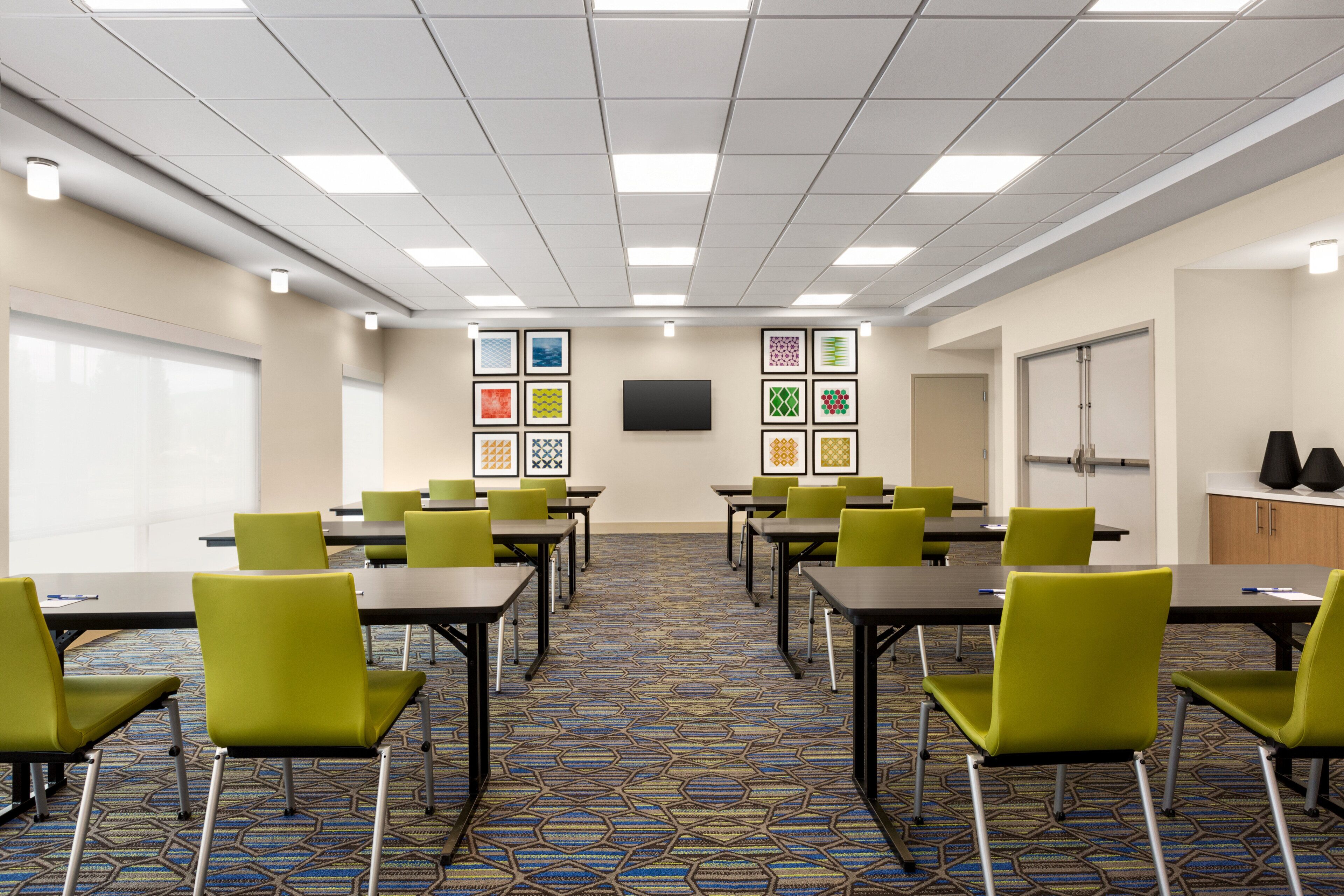 A conference room with multiple tables and chairs, a patterned carpet, and framed artwork on the walls.